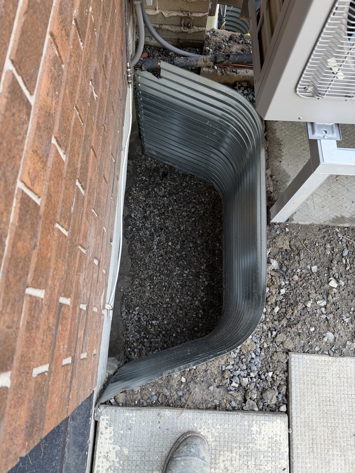 New window well and drainage installation beside a brick home